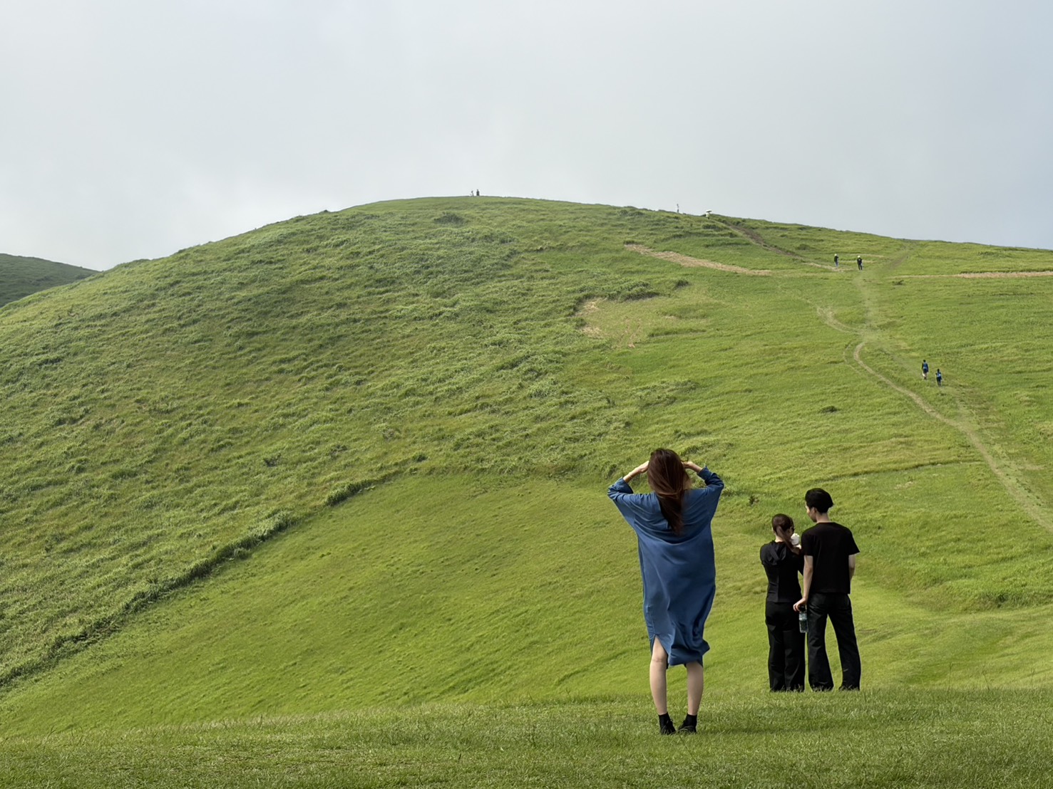 緑豊かな丘を見上げる人々と山頂へ続く細い道